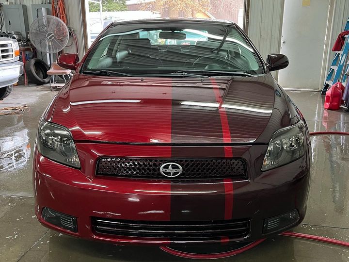Red Scion tC in the shop with a fresh dark center stripe over the hood and roof