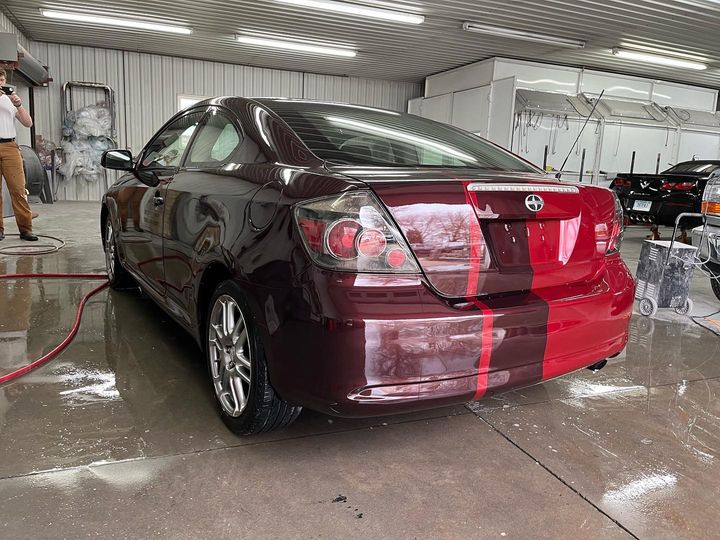 Rear of the red Scion tC in the shop, the dark stripe running over the trunk and bumper