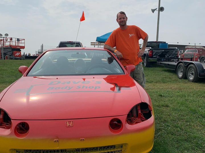 Red and yellow race car lettered Dave's Body Shop on the hood, in the pits with a crew member in an orange shirt